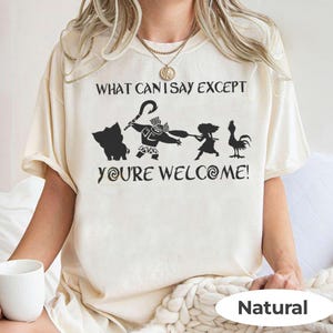 Puede incluir: Camiseta color crema con un gr&aacute;fico negro que presenta personajes y texto de una popular pel&iacute;cula de animaci&oacute;n. El texto dice "WHAT CAN I SAY EXCEPT YOU'RE WELCOME!". La camiseta est&aacute; etiquetada como "Natural" en la parte inferior.