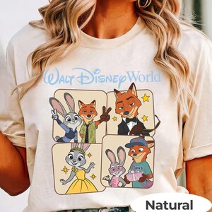 Puede incluir: Camiseta beige con un gr&aacute;fico de personajes de Zootopia y el texto "Walt Disney World" en azul claro. El dise&ntilde;o incluye a Judy Hopps y Nick Wilde en varias poses. La palabra "Natural" est&aacute; impresa en la parte inferior.
