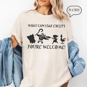 Puede incluir: Camiseta de color marfil con un gr&aacute;fico negro que presenta personajes y texto de una popular pel&iacute;cula de animaci&oacute;n. El texto dice "WHAT CAN I SAY EXCEPT YOU'RE WELCOME!". Una burbuja de di&aacute;logo en la esquina superior derecha dice "IVORY".