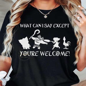 Puede incluir: Camiseta negra con un gr&aacute;fico blanco de personajes y el texto "WHAT CAN I SAY EXCEPT YOU'RE WELCOME!". El dise&ntilde;o incluye un cerdo, un personaje con un gancho, una ni&ntilde;a y un gallo. La camiseta es de cuello redondo.