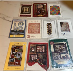 May include: A collection of quilt pattern packets in plastic sleeves. The packets feature various quilt designs, including geometric patterns, horses, and holiday themes. Text includes "Gathering Friends", "Quilt Tales", and "Just Horses".