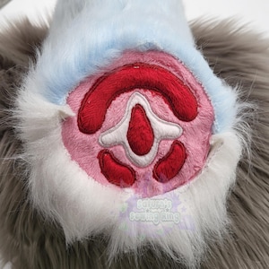 Può includere: Primo piano di un cuscinetto zampa in peluche con centro rosa, dettagli rossi e dettagli bianchi. La zampa è circondata da finta pelliccia grigia e bianca, con un bordo azzurro. Il testo "Saturn's sewing king" è visibile.