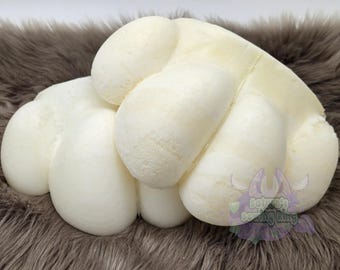 May include: A white, rounded, multi-lobed foam structure resembling a stylized animal paw. The object has a smooth, matte surface with several distinct, plump, cushion-like sections. A small purple logo with the text Saturn's Sewing King is visible.