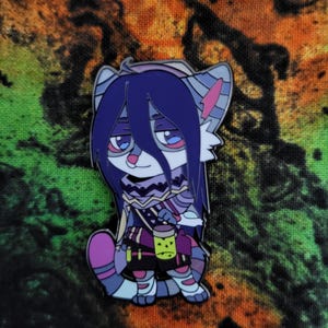 May include: A purple and white enamel pin of a furry creature with long purple hair, wearing a purple and yellow scarf and holding a green and yellow container. The pin is on a colourful background.