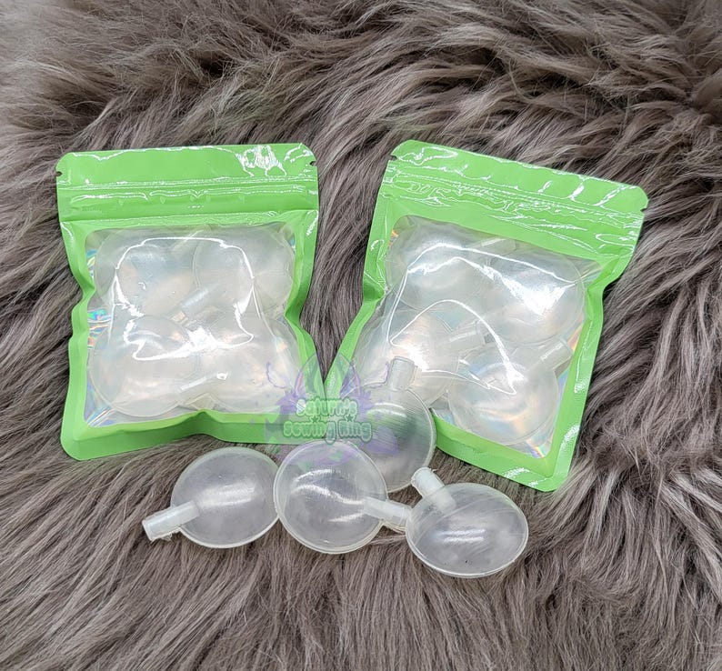 May include: Clear, bulb-shaped silicone applicators with a small nozzle, packaged in green-edged, clear plastic bags. Several applicators are also visible outside the bags. The items are on a gray, furry surface.