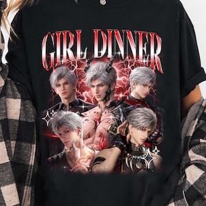 Può includere: T-shirt nero a maniche lunghe con la scritta "GIRL DINNER" in rosso e bianco. La maglietta presenta una grafica di cinque personaggi in stile anime con capelli argentati e uno sfondo di fulmini rossi.