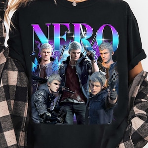 Peut inclure: T-shirt noir avec le mot "NERO" dans une police multicolore. Le t-shirt présente un collage d'images d'un personnage aux cheveux argentés et portant diverses tenues, tenant des armes. Le design a une esthétique rétro et néon.