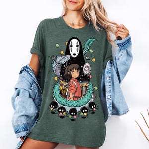 Może przedstawiać: Zielona koszulka z nadrukiem postaci z filmu animowanego Spirited Away. Postacie to Chihiro, Bez Twarzy i duch rzeki.