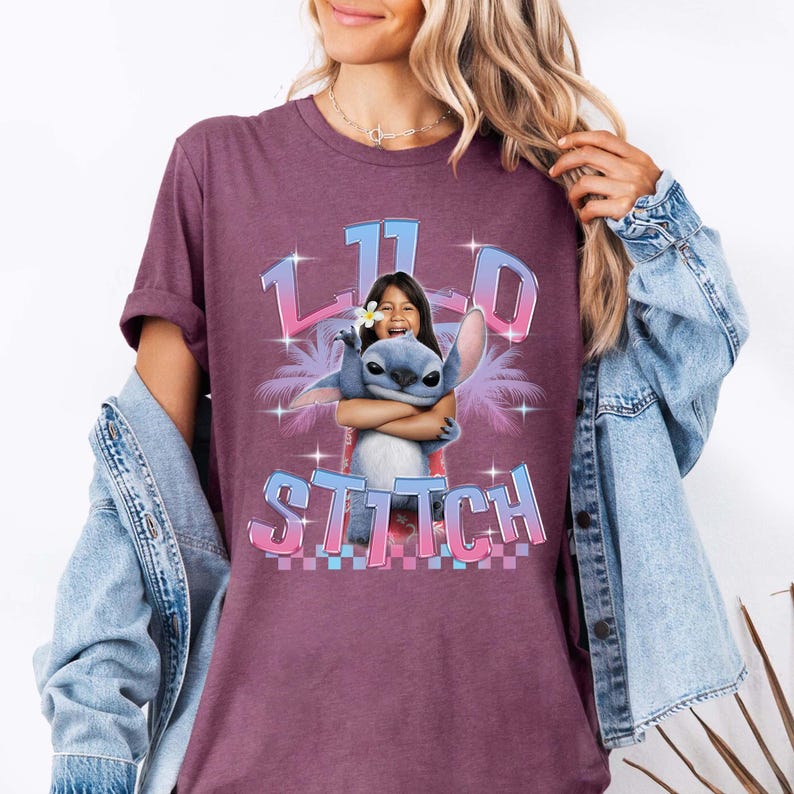 Pode incluir: Camiseta bord&ocirc; com um desenho de Stitch de Lilo & Stitch abra&ccedil;ando uma menina. O design inclui o texto "11.0 Stitch" em uma fonte gradiente, palmeiras e estrelas.