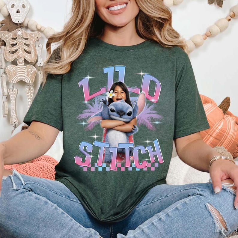 Pode incluir: T-shirt verde escuro com um gr&aacute;fico de uma menina abra&ccedil;ando o personagem Stitch. O design inclui o texto "110 Stitch" em uma fonte colorida e estilizada. A camiseta tem um corte folgado.