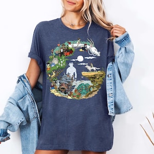 K&ouml;nnte beinhalten: Marineblaues T-Shirt mit einer farbenfrohen Illustration einer Fantasielandschaft. Es zeigt einen wei&szlig;en Drachen, Geb&auml;ude und Charaktere. Das kreisf&ouml;rmige Design zeigt verschiedene Elemente einer Fantasiewelt. Das T-Shirt ist aus weichem Material.