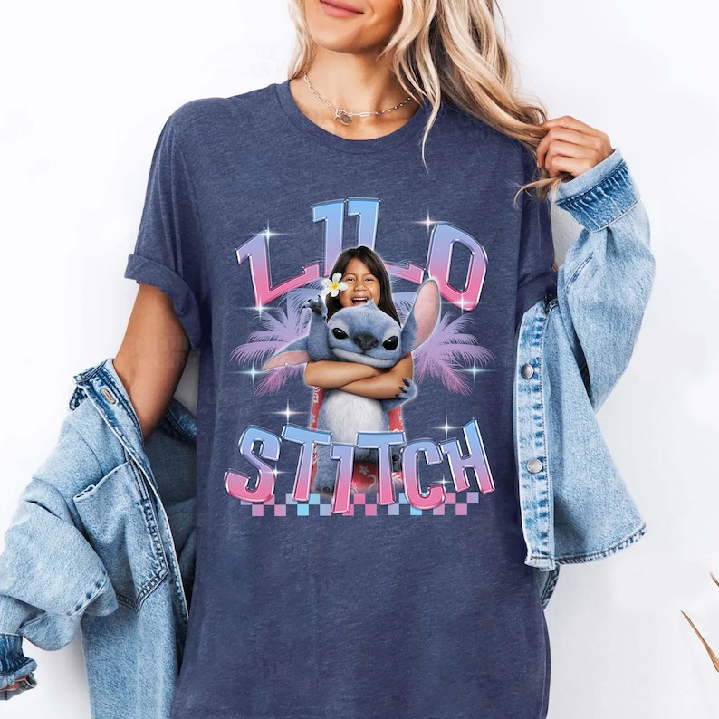 Pode incluir: Uma camiseta azul marinho com um gr&aacute;fico de uma menina abra&ccedil;ando o personagem Stitch do filme Lilo & Stitch. O gr&aacute;fico inclui o texto "11" e "Stitch" em um design tropical colorido. A camiseta tem mangas curtas.