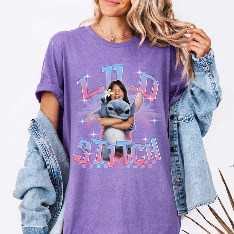 Pode incluir: Uma camiseta roxa com um gr&aacute;fico de uma menina abra&ccedil;ando o personagem Stitch. O gr&aacute;fico inclui o texto "11" e "Stitch" em uma fonte colorida e estilizada. A camiseta tem mangas curtas e um corte folgado.