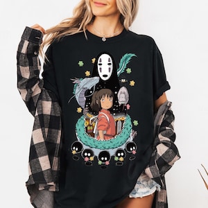 Może przedstawiać: Czarny T-shirt z nadrukiem graficznym postaci z filmu animowanego Spirited Away. Postać to biały, bez twarzy duch z długimi czarnymi włosami. Postać jest otoczona zielonym, liściastym winoroślą i małymi czarnymi stworzeniami. Tekst "Spirited Away" nie jest widoczny na obrazku.