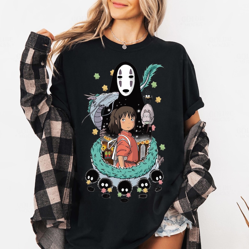 Może przedstawiać: Czarny T-shirt z nadrukiem graficznym postaci z filmu animowanego Spirited Away. Postać to biały, bez twarzy duch z długimi czarnymi włosami. Postać jest otoczona zielonym, liściastym winoroślą i małymi czarnymi stworzeniami. Tekst "Spirited Away" nie jest widoczny na obrazku.