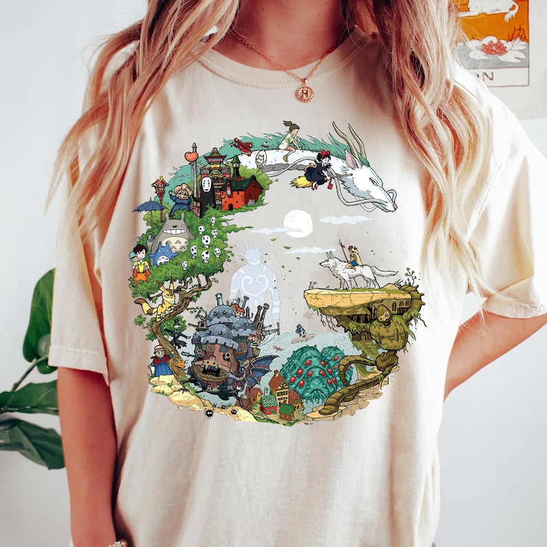 K&ouml;nnte beinhalten: Cremefarbenes T-Shirt mit einem kreisf&ouml;rmigen Grafikdesign mit animierten Charakteren und Szenen. Das Design umfasst einen wei&szlig;en Drachen, ein M&auml;dchen auf einem Besen und verschiedene Geb&auml;ude und Kreaturen in einer farbenfrohen, detaillierten Illustration.