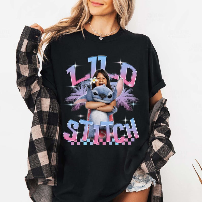 Pode incluir: T-shirt preto com um design gr&aacute;fico colorido de Stitch abra&ccedil;ando uma menina, com o texto "11th Stitch". O design inclui palmeiras e estrelas. A fonte &eacute; um gradiente. Uma camiseta divertida e casual.