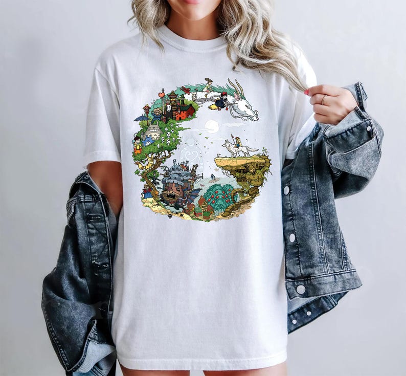 K&ouml;nnte beinhalten: Wei&szlig;es T-Shirt mit einem farbenfrohen Grafikdesign einer Fantasielandschaft mit verschiedenen Charakteren und Kreaturen. Das Design umfasst einen Drachen, ein Schloss und andere Elemente, wodurch eine skurrile und detaillierte Szene entsteht. Das Shirt ist ein Freizeitkleidungsst&uuml;ck.