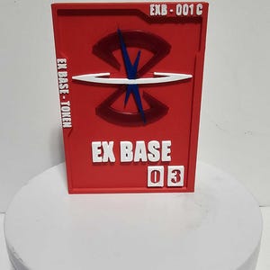 K&ouml;nnte beinhalten: Ein rechteckiger roter Token mit dem Text EXB-001C oben rechts, EX BASE-TOKEN auf der linken Seite und EX BASE 03 unten. In der Mitte befindet sich ein erhabenes dunkelrotes kreisf&ouml;rmiges Emblem mit einer blauen vertikalen und einer wei&szlig;en horizontalen Linie.
