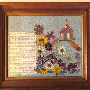 Pu&ograve; includere: Opera d'arte incorniciata con fiori secchi, spartiti e una chiesa in miniatura. La cornice in legno circonda uno sfondo azzurro con un motivo floreale. Il testo "The Church in the Wildwood" &egrave; visibile.