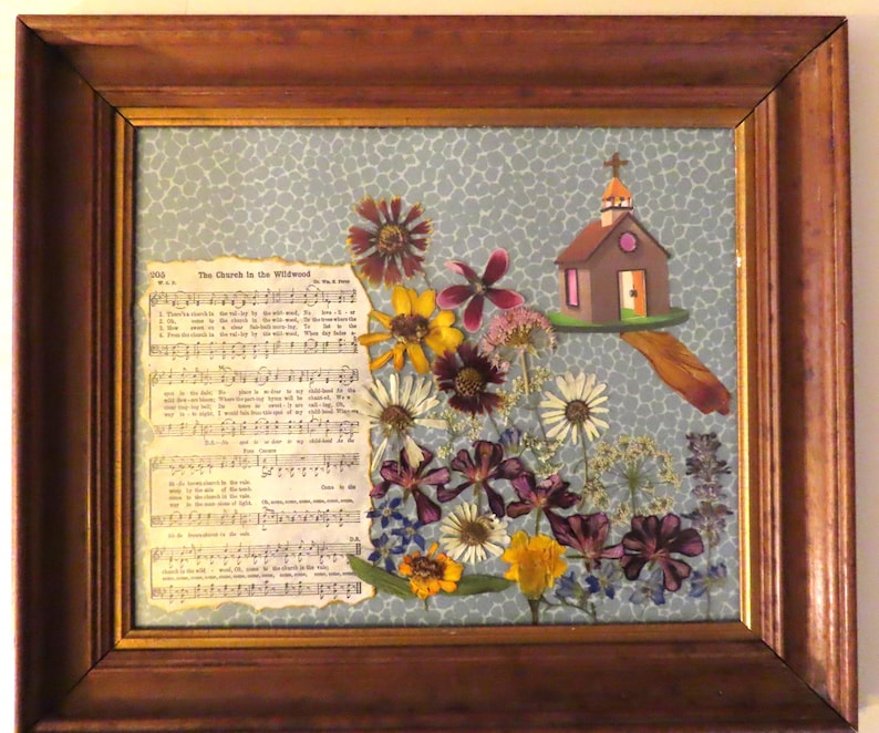 Pu&ograve; includere: Opera d'arte incorniciata con fiori secchi, spartiti e una chiesa in miniatura. La cornice in legno circonda uno sfondo azzurro con un motivo floreale. Il testo "The Church in the Wildwood" &egrave; visibile.