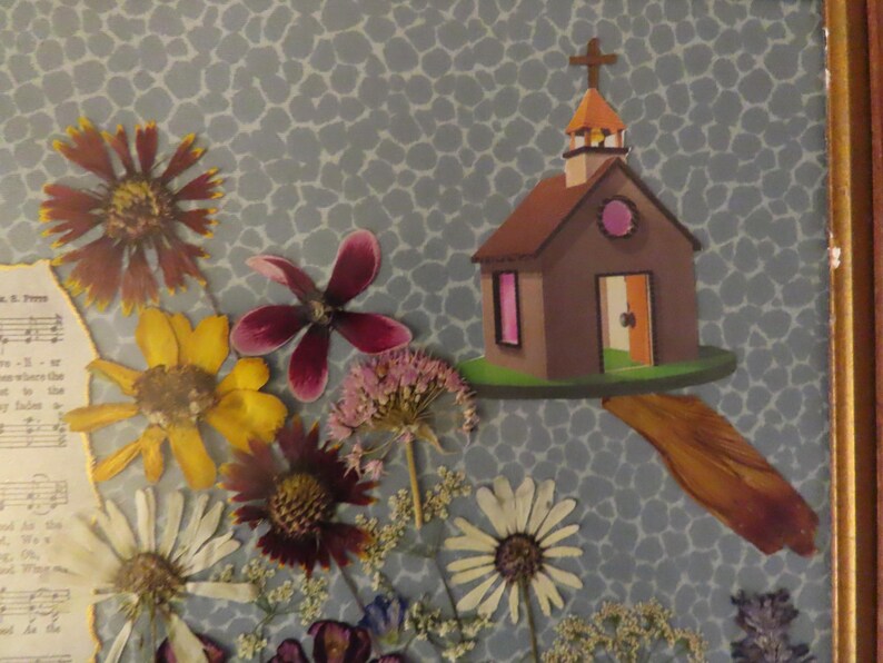 Pu&ograve; includere: Un collage incorniciato con una chiesa di carta con una croce, circondata da fiori pressati di vari colori. Lo sfondo &egrave; una carta blu a motivi e uno spartito musicale &egrave; visibile.