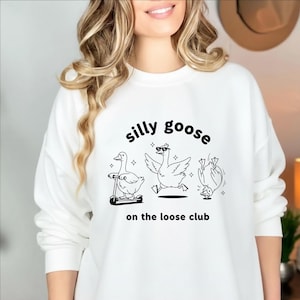 May include: White sweatshirt with the text "silly goose" above three cartoon geese. One goose rides a scooter, another wears sunglasses, and the third does a handstand. The phrase "on the loose club" is below the geese.