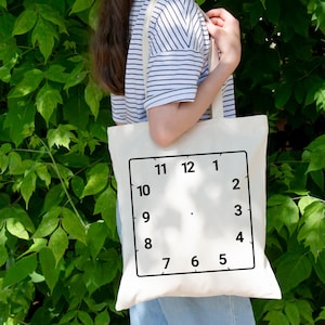 May include: A white tote bag with a black clock face design. The clock face has black numbers 1 through 12.