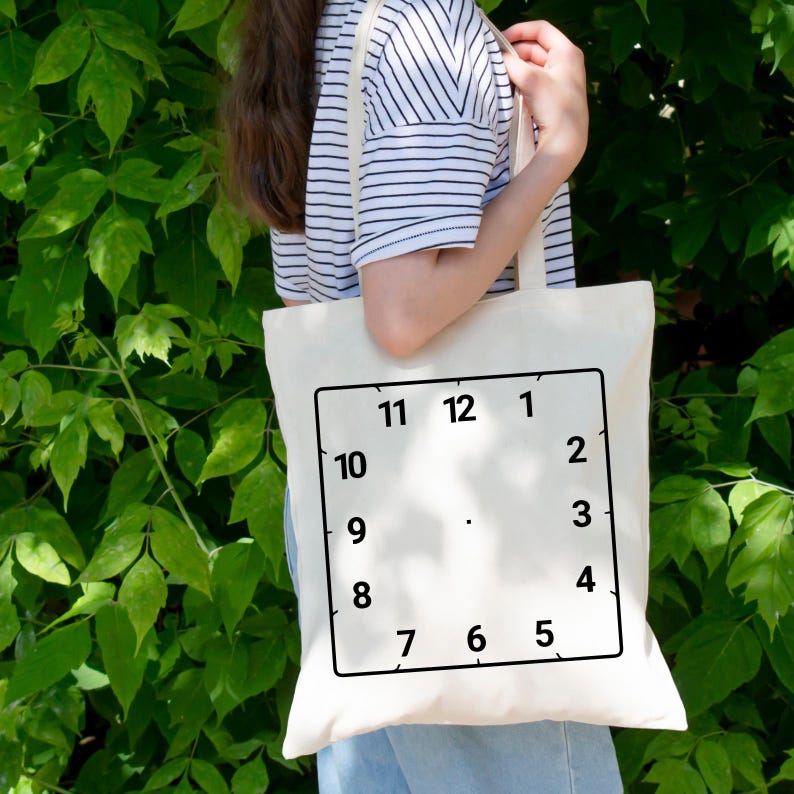 May include: A white tote bag with a black clock face design. The clock face has black numbers 1 through 12.