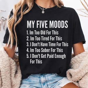 May include: A black short-sleeved t-shirt featuring the white text MY FIVE MOODS followed by a numbered list: 1. Im Too Old For This, 2. Im Too Tired For This, 3. I Don't Have Time For This, 4. Im Too Sober For This, 5. I Don't Get Paid Enough For This.