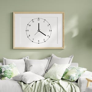 May include: A framed print of a black and white clock face with the numbers 1 through 12 and hands pointing to 3 o'clock. The clock is hanging on a light green wall above a white couch with green pillows.