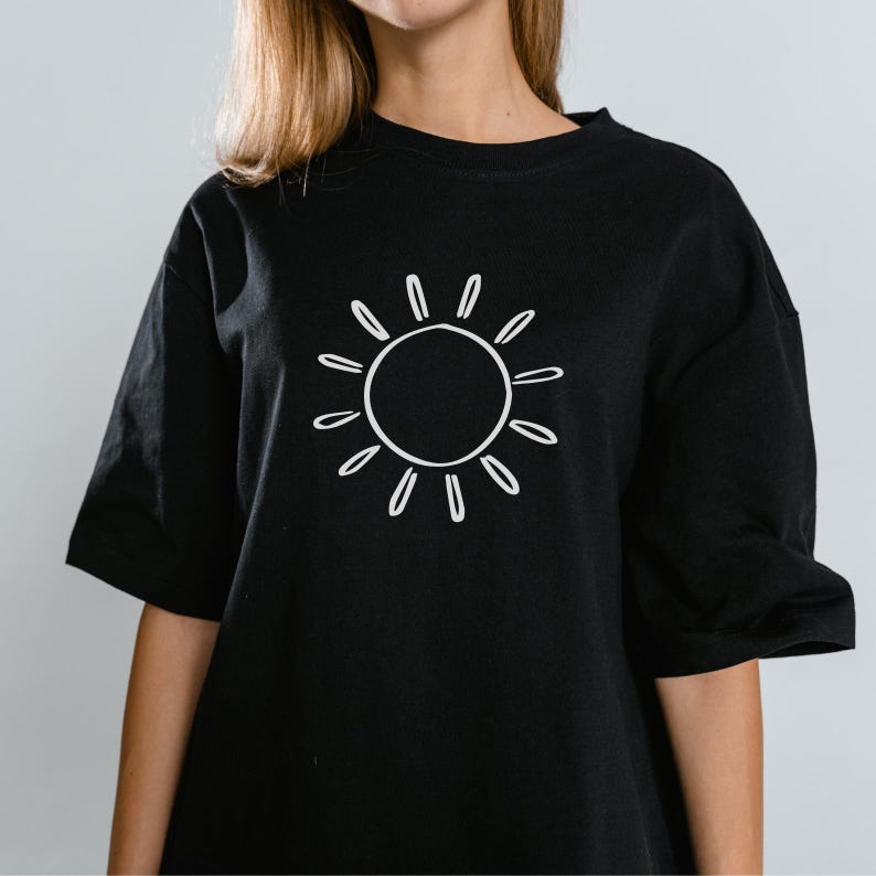 Może przedstawiać: Czarny t-shirt z białą grafiką słońca. Projekt słońca to prosty kontur z okrągłym środkiem i promienistymi liniami. Koszulka ma kr&oacute;tkie rękawy i okrągły dekolt.