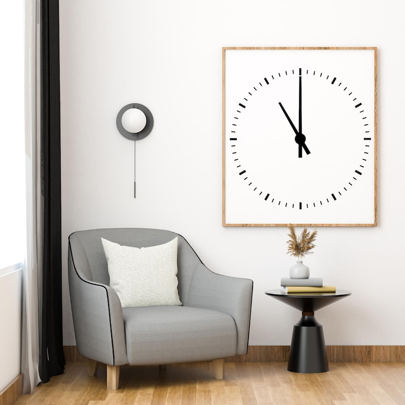 May include: A gray armchair with a white pillow sits in a living room with a black and white clock on the wall, a small black side table with a vase of dried flowers, and a white wall lamp.