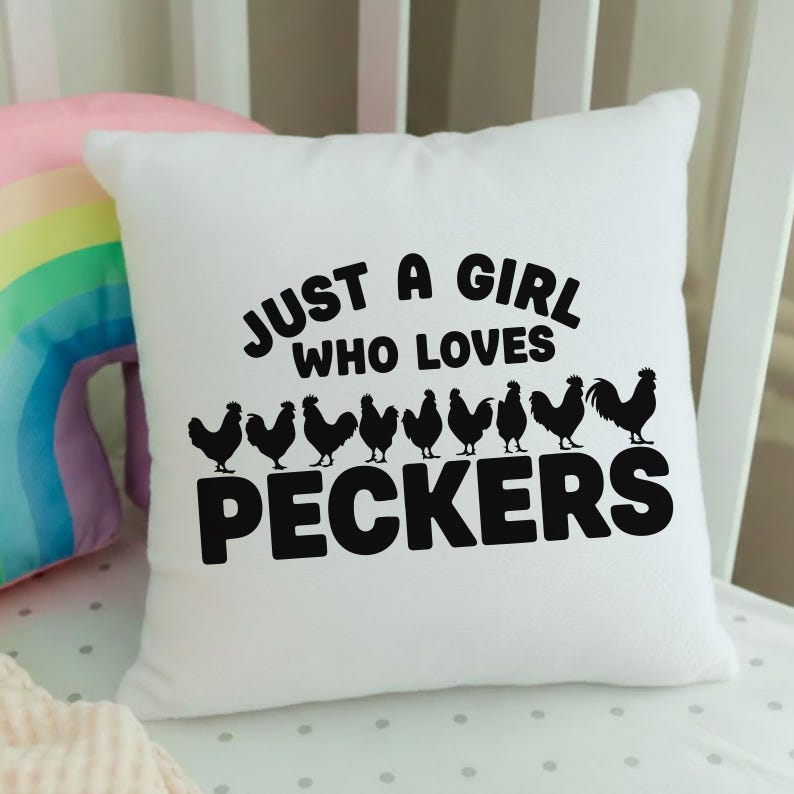 May include: White square pillow with the text "JUST A GIRL WHO LOVES PECKERS" in black. Below the text are black silhouettes of chickens. The pillow is on a white crib.