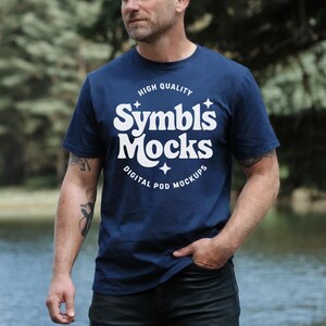 Pode incluir: Camiseta azul marinho com texto branco. O texto diz "Symbls Mocks", "High Quality" e "Digital Pod Mockups". A camiseta tem mangas curtas e gola redonda.