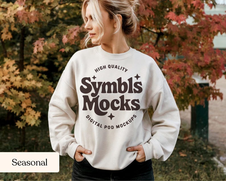 May include: Cream-colored sweatshirt with the text "Symbls Mocks" in brown, surrounded by stars and the words "High Quality" and "Digital Pod Mockups". The sweatshirt is worn by a person standing outdoors.
