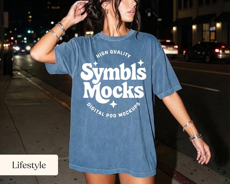 May include: A blue t-shirt with the text "Symbls Mocks" in white, with the words "High Quality" above and "Digital Pod Mockups" below. The shirt is worn by a person on a city street at night.