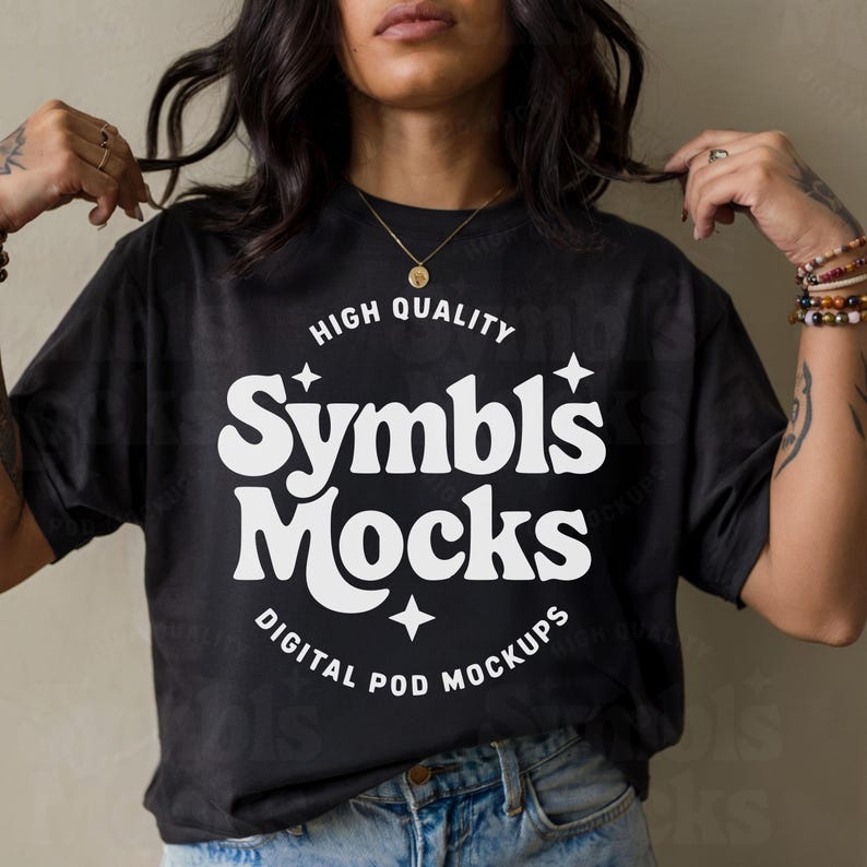 May include: Black t-shirt with the text "HIGH QUALITY Symbl's Mocks DIGITAL POD MOCKUPS" in white. The shirt is worn by a person with dark hair and blue jeans. The shirt has a round neckline.