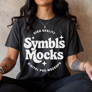 Może przedstawiać: Czarny t-shirt z białym napisem "Symbl's Mocks". Koszulka zawiera również białe słowa "High Quality" i "Digital Pod Mockups". Modelka ma na sobie złoty naszyjnik i bransoletki.