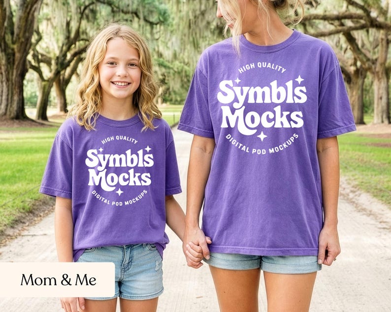 May include: Two people wearing matching purple t-shirts with the text "Symbls Mocks" in white. The shirts are paired with denim shorts. The phrase "Mom & Me" is at the bottom of the image.