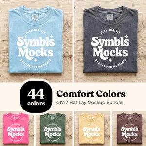 May include: A flat lay mockup bundle featuring folded t-shirts in various colors, including light blue and charcoal gray. The shirts display the text "Symbls Mocks" and "Digital Pod Mockups". The image also includes text that says "44 colors" and "Comfort Colors C1717 Flat Lay Mockup Bundle."