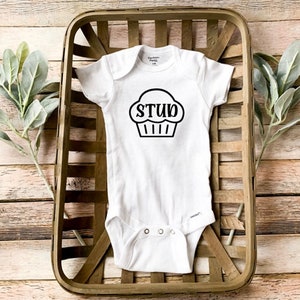 May include: White baby onesie with a black cupcake graphic and the word "STUD" printed on the cupcake.