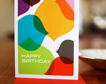 Puede incluir: Una tarjeta de cumpleaños colorida con formas abstractas superpuestas en tonos de verde, azul, amarillo, rojo, morado y marrón. La tarjeta dice "Feliz cumpleaños".