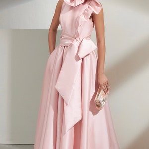 May include: A sleeveless pink satin gown with a large ruffled collar and a matching sash tied in a bow at the waist. The gown has a full skirt and is floor-length.