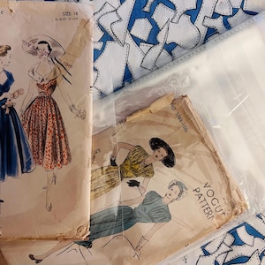 May include: Vintage Vogue sewing patterns featuring illustrations of women in dresses. The patterns are in aged paper packaging, with the text "Vogue Pattern" visible. The image includes a blue and white patterned fabric.