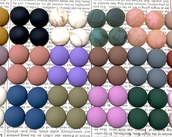 Könnte beinhalten: Sortiment von 40 runden, flachen, bunten Cabochons. Die Cabochons sind in Reihen zu zweit angeordnet, wobei jede Reihe eine andere Farbe aufweist. Die Farben umfassen Weiß, Beige, Hellbraun, Dunkelbraun, Grau, Lila, Rosa, Grün und Blau.
