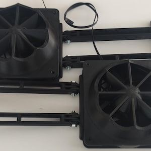 May include: Two black computer fans with a radial blade design are shown. Each fan is square and mounted on a black bracket with mounting holes. A black wire extends from each fan. The fans are likely for cooling computer components.