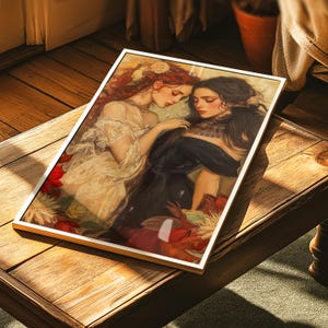 May include: A framed art print featuring a romantic scene of two women. One woman has long red hair and wears a cream-colored dress, while the other has black hair and a black dress. The artwork is set against a floral background.