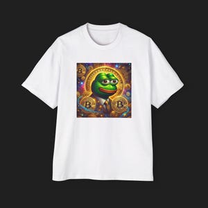 May include: White t-shirt featuring a colorful graphic of a green frog wearing a suit, surrounded by gold Bitcoin symbols. The frog has a red mouth and is set against a vibrant, detailed background. The shirt is made of a soft material.