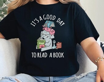 May include: Black t-shirt with the text "IT'S A GOOD DAY TO READ A BOOK". The graphic features an elephant reading a book, with a pig and other books stacked on top. The elephant is wearing glasses.